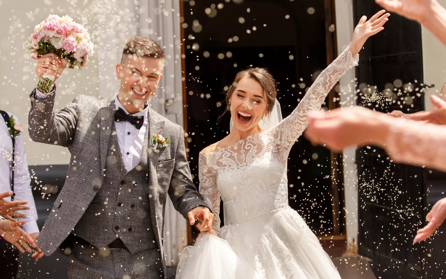 Newlyweds smiling and celebrating outside after their wedding, surrounded by confetti and holding hands.