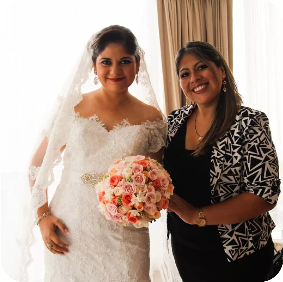 Magaly Ponce in black poses with the bride in her wedding dress holding a pink and orange bouquet.